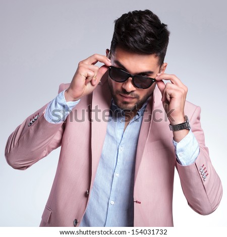 young fashion man taking off his sunglasses while looking into the camera. on a light background