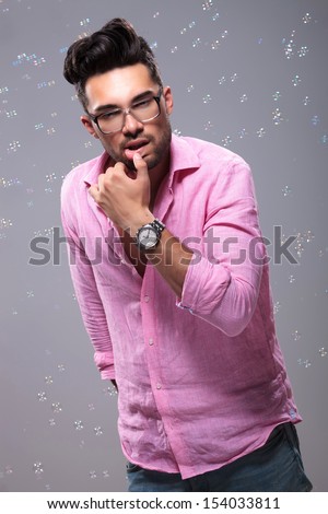 young fashion man sensually touching his lower lip with hi thumb while bubbles float around him. on a gray background