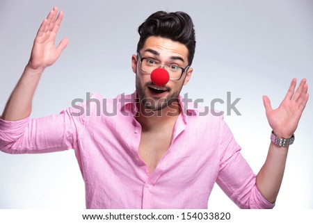 young fashion man with a red nose making gesures with his hands while looking into the camera. on a light background