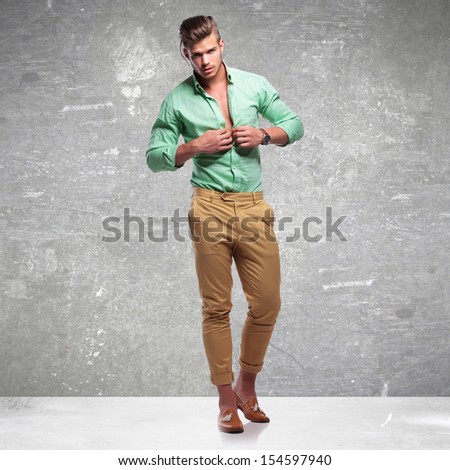 full length photo of a young casual man taking his shirt off while looking into the camera. on gray  vigneta light background