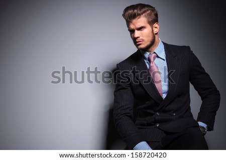 seated young fashion model in suit and tie is looking away to his side