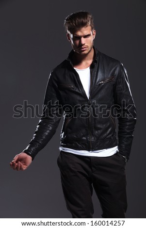 young fashion male model in leather jacket posing with his hand out on a dark background