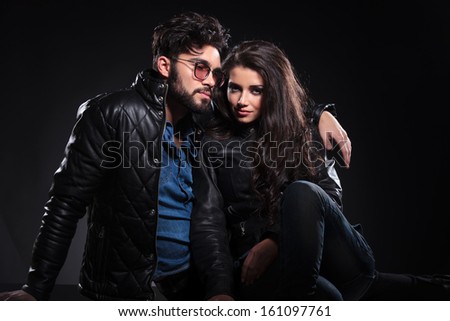 young fashion couple on dark background, woman looking at the camera and man looking pensive to a side