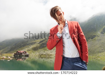 fashion man pulling his hair in front of a mountain lake with cabin