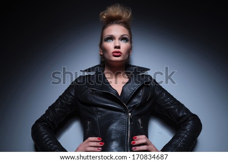 young sexy blonde woman in leather jacket standing with hands on hips and looking up