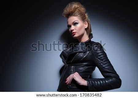 young beauty woman in leather clothes standing with hands on hips and looking away to her side