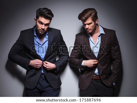serious men posing in studio, one buttoning his coat, one looking away