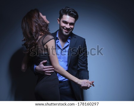 portrait of a young fashion couple dancing while the man smiles for the camera and the woman laughs away. on a dark blue background
