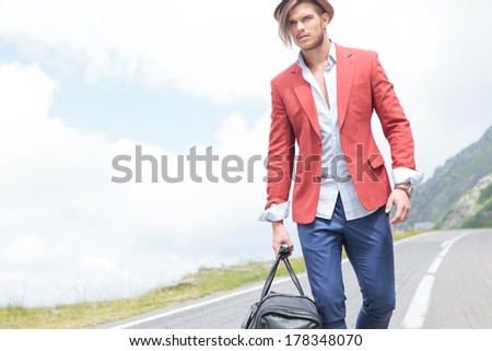 picture of a young fashion man carrying a voyage bag outdoor, while looking away from the camera