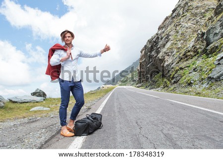 portrait of a young fashion man hitchhiking in the mountains with a smile on his face