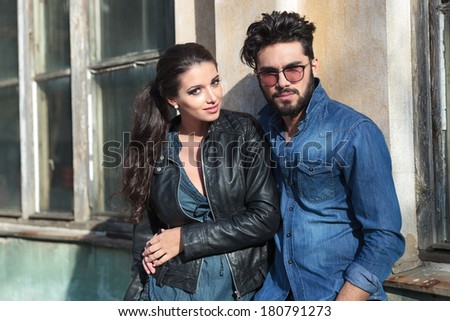portrait of a young casual couple embracing outdoor, by an old building while looking into the camera