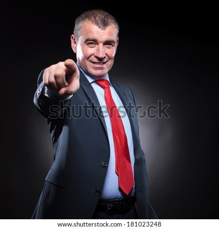 smiling old business man pointing his finger to the camera on black studio background