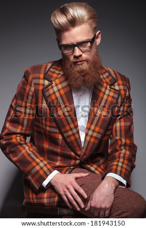 dramatic fashion model with long beard and glasses sitting and looks at the camera