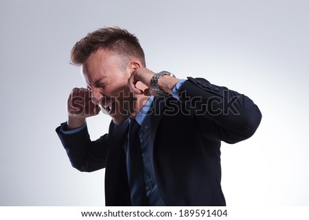 young business man plugging his ears with his fingers and closing his eyes while screaming. on a light gray studio background