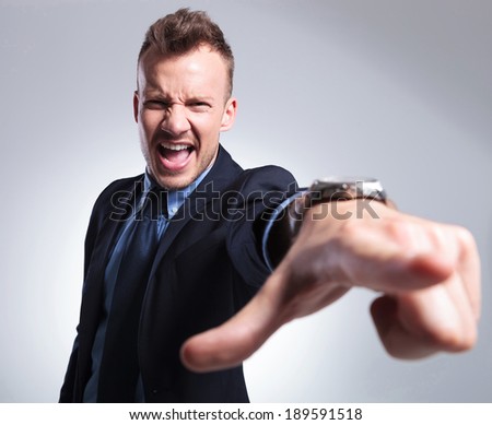 angry young business man shouting and pointing at the camera. gray background