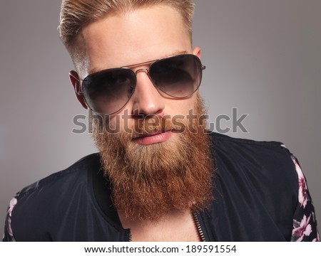 close up picture of a casual young man with a long red beard, looking into the camera. on gray studio background