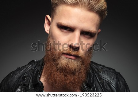 close up of a casual young man with a hipster beard, looking into the camera. on a dark studio background