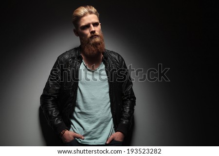 casual young man with his hands in his pockets looking away from the camera. on a dark studio background