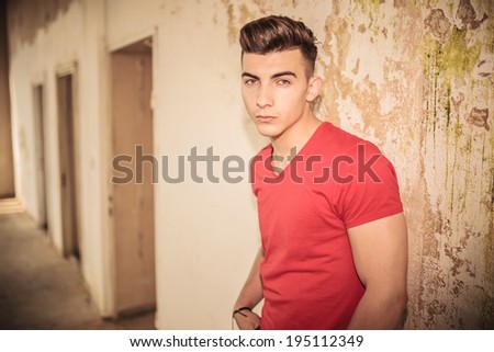 sad man leaning against a dirty wall in an old room