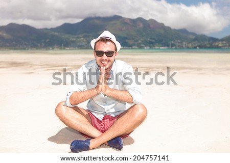 young man sits on the beach and prays for more sun in his vacation