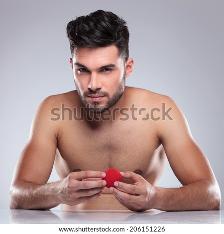 naked young man holding a red ball looking to the camera