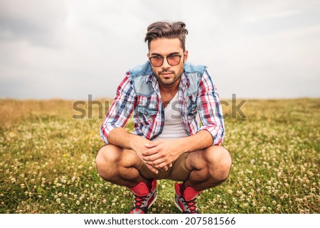 serious crouched casual man in a field of grass looks to the camera