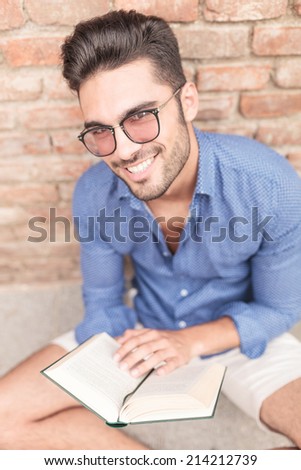 seated casual man with glasses holding a book and smiles to the camera
