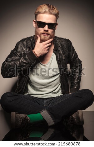 Fashion man in leather jacket looking down, sitting and holding his hands, studio shot