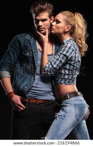 Hot blonde woman trying to kiss her boyfriend on the cheek. The man is holding one hand in his pocket, looking away.