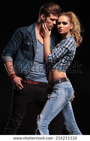 Attractive blonde woman posing for the camera while holding her boyfriend chin. The man is holding his hand in his pocket, looking away.