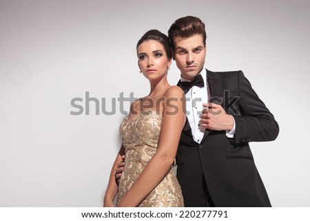 Elegant fashion couple posing on grey studio background, the woman wearing an elegant dress is leaning on her lover.