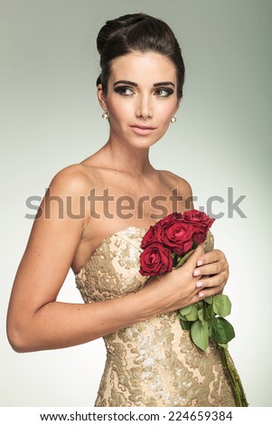 Side view of an elegant woman in dress holding red roses and looks away from the camera in studio