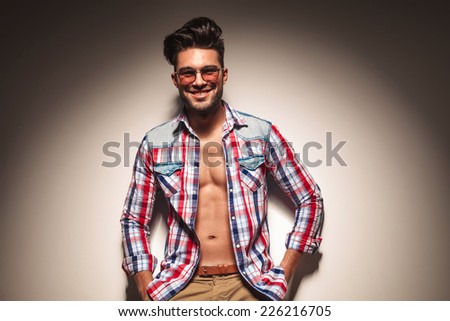 Picture of a sexy young fashion man leaning on a wall while holding his hands in pocket.