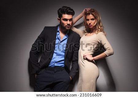 Young fashion business man looking away with his hands in pockets while his lover is leaning on him and fixing her hair.
