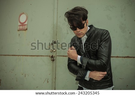 Handsome young fashion man looking down while fixing his jacket, near a metal gate.