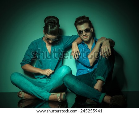 Fashion woman looking down and  arranging her shirt while her lover is sitting next to her looking at the camera.