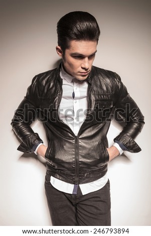 fashion man leaning on a white wall holding his hands in pockets while looking down.