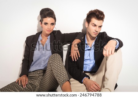 Beautiful fashion woman sitting next to her boyfriend, leaning her arm on his shoulder while he is looking away.