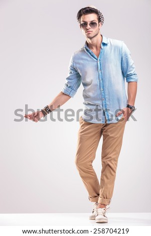 Young casual man posing on grey studio background while snapping his fingers, full body picture.
