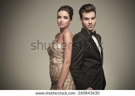 Elegant man and woman standing back to back on grey studio background.