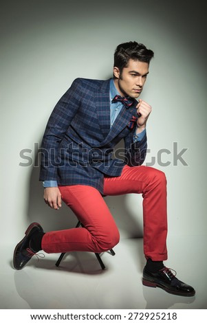 Full body picture of a handsome young fashion man sitting on a chair with his legs apart.