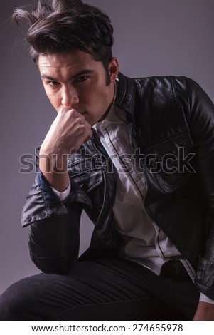 Portrait of a casual fashion man looking at the camera while holding his hand to his mouth.