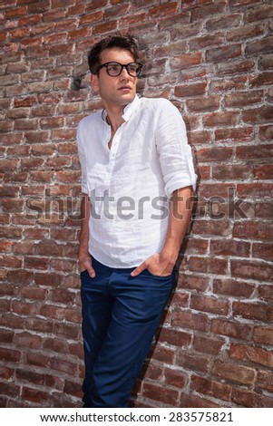 Portrait of a handsome fashion man leaning on a brick wall while holding his hands in pockets.