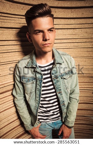 side view of a casual young man in jeans jacket looking away against wooden background