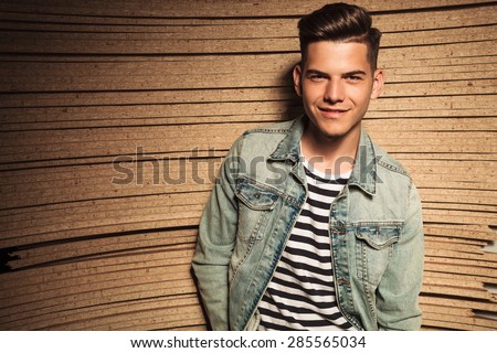 happy young casual man in jeans jacket smiles against wooden background