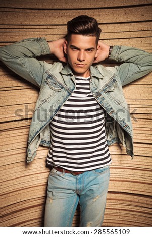 cool relaxed casual young man holding his hands behind his neck against wooden background in studio