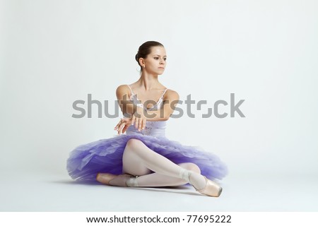 graceful ballet dancer with purple tutu sitting on studio background