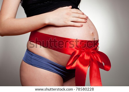 Pregnant belly with red ribbon. Nine month. Third trimester