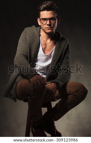 Handsome casual man holding one hand on his knee while sitting on a stool.