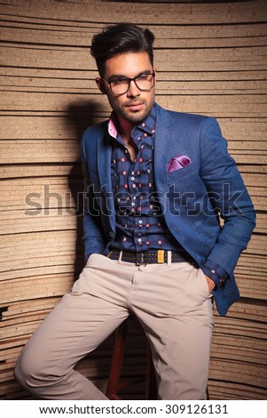 Handsome young fashion man leaning on a chair while holding his hand in pockets.